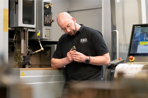 Mitarbeiter im schwarzen JUNO-Poloshirt prüft ein Metallteil an einer Maschine
